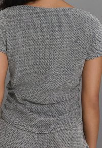 Haut gris texturé avec un motif subtil, manches courtes et coupe décontractée. Le tissu semble doux avec une légère élasticité.