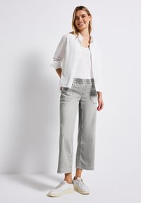Chemise blanche légère à boutons sur un débardeur blanc, associée à un pantalon large gris clair avec une taille élastique et des poches latérales.
