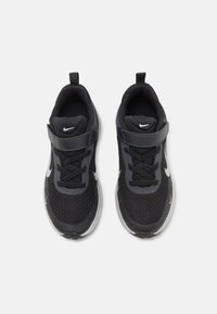 Baskets de sport noires avec un design en mesh, des accents synthétiques, une forme courbée et un logo swoosh réfléchissant. Caractéristiques : lacets et une bandoulière en Velcro.
