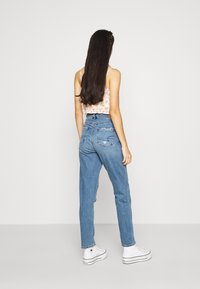 Jeans de mezclilla azul de talle alto y corte holgado, con bolsillos traseros y un ligero desgastado, combinados con zapatillas de lona blancas.