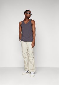 Top gris de tirantes, pantalones holgados beis claros y zapatillas blancas con rayas negras. Las gafas de sol completan el atuendo casual.