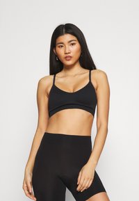 Svart bralette med tynne stropper, myk tekstur og scoop-hals, sammen med svarte høytaljede shorts. Minimalistisk design, ingen synlig maskinvare.