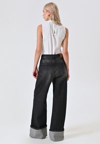 Wit mouwloos topje met een sleutelgatdetail aan de achterkant. Zwarte wijde jeans met opgerolde grijze omslagen en een achterzak.