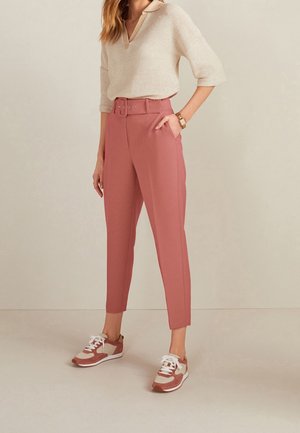 Pantalons rose ajustés mi-hauts avec une taille ceinturée. Associés à un top en tricot crème et des baskets brunes avec des accents blancs et beiges.