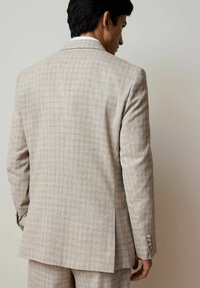 Light beige checkered suit jacket featuring a two-button closure, notch lapels, side vents, and detailed button accents on the cuffs.