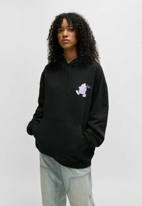 Felpa nera con cappuccio e tasca frontale, con lacci e una grafica colorata sul lato sinistro del petto. Presenta polsini e orlo a coste, vestibilità comoda.