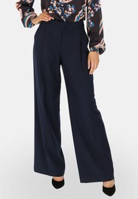 Granatowe spodnie szerokie o dopasowanym kroju, z wysokim pasem i gładką fakturą materiału. Wykończone wyraźnymi fałdami z przodu.