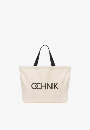 Kremowa torba na ramię z czarnymi rączkami i wyraźnym czarnym logo "OCHNIK" nadrukowanym na środku z przodu.