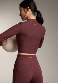 Bourgondisch geribd cropped top met lange mouwen, gecombineerd met hooggetailleerde leggings, beide met een klein logo op de achterkant. Gestructureerde stof.