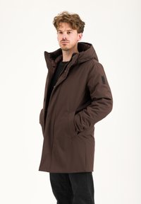 Cappotto marrone con cappuccio, caratterizzato da un esterno liscio e texturizzato e un interno trapuntato. Presenta tasche laterali e una discreta etichetta del marchio sulla manica.