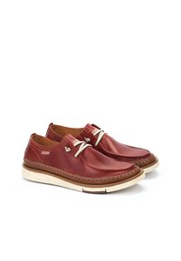 Chaussures en cuir rouge avec un bout arrondi, dotées de coutures décoratives, de lacets beiges et d'une semelle texturée crème et marron.
