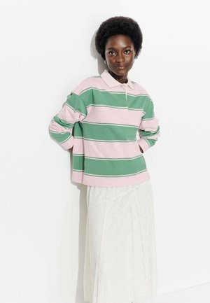 Polo à manches longues rayé rose et vert avec un col, associé à une jupe en dentelle blanche, présenté sur un fond blanc uni.