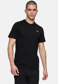 Svart kortärmad t-shirt i bomull med rund halsringning och röd FILA-logotyp på vänster bröst. Har en normal passform och en mjuk textur.