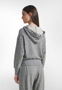 Felpa grigia in pile con cappuccio regolabile con coulisse, polsini a costine e orlo a costine. Texture morbida, vestibilità comoda e motivo melange discreto.