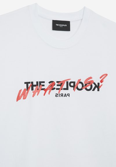 White cotton t-shirt featuring bold black and red text. The design includes "THE KOOPLES" and "WHAT IS?" in stylized fonts.