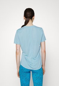 Camiseta atlética de mangas cortas en azul claro con un escote redondo y una costura sutil en la parte posterior, combinada con leggings azules que presentan un patrón de lunares negros.