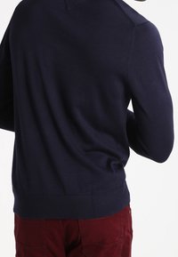 Pull bleu marine avec un ourlet et des poignets côtelés, coupe ajustée, présentant une texture lisse ; affiché de dos sur un fond blanc.