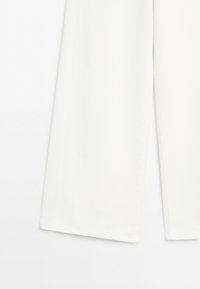 Lower section of white wide-leg pants with a clean, smooth fabric and straight hems against a plain background.