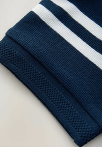 Tissu bleu marine foncé avec des rayures blanches et bleu clair, présentant une surface texturée et un ourlet détaillé et à motifs.