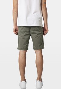 Pantaloni scurți din bumbac de culoare verde măsliniu, cu margini rulante și buzunare laterale, asortați cu un tricou alb și adidași albi. Accent pe un design casual.