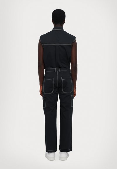 Black sleeveless shirt with contrasting white stitching, paired with black cargo pants featuring side pockets and a straight-leg cut.