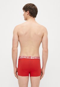 Punased bokserpüksid valge elastse vöökohaga, millel on "DIESEL" logo. Sile kangas, vormis disain ja lühike säärepikkus. Tagantvaade.