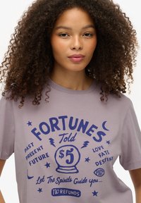 Camiseta de algodón morada con un diseño gráfico de una bola de cristal, estrellas y texto sobre la adivinación en tinta azul marino.