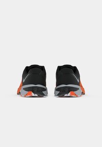 Pair of black and orange Nike Metcon sneakers shown from the back on a white background.