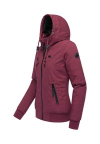 Burgunderfarget hettegenser med strukturert stoff, to glidelåslommer på sidene, justerbare snorer og et sirkulært logo-patch på ermet.