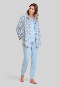 Conjunto de pijama de felpa azul con chaqueta de estampado de lunares, parte superior azul a juego y pantalones con lunares. Textura suave, mangas largas y puños elásticos.
