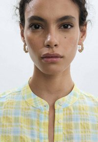 Camicia button-up con un motivo a quadri giallo e azzurro chiaro, colletto rotondo e texture delicata. Presenta due bottoni nella parte anteriore.