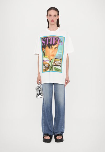 White oversized t-shirt with colorful graphic print, paired with light blue wide-leg jeans and black platform sandals. Silver handbag.
