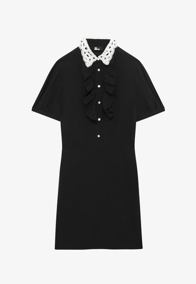 Rochie neagră cu mâneci scurte, față volanată, guler din dantelă albă și detalii cu nasturi aurii. Țesătură netedă cu o siluetă structuratã.