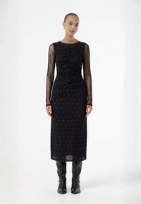Μαύρο φόρεμα με διάφανα μακριά μανίκια, λεπτομέρεια νούλας στη μέση και ασημένιες κουκίδες σε όλη την επιφάνεια. Φορεμένο με μαύρες μπότες μέχρι το γόνατο.