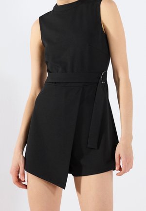 Schwarzer ärmelloser Jumpsuit mit hohem Kragen, ausgestattet mit einem taillierten Gürtel, einem einzigartigen Wickeldesign und einer glatten Stofftextur.