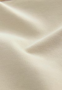 Tissu beige texturé avec une surface douce et lisse, présentant un motif côtelé subtil. Le matériau semble léger et souple.