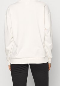 Felpa crema a maniche lunghe con vestibilità rilassata, polsini e orlo a coste, e una texture liscia, abbinata a leggings scuri.