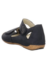 Chaussure en cuir noir au design ouvert, avec découpes latérales et fermeture à pression. Semelle en liège avec des coutures visibles autour du bord.