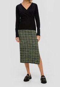 Czarna, długosleeve, owijana bluzka w połączeniu z zieloną wzorzystą spódnicą midi z abstrakcyjnymi wzorami i bocznym rozcięciem; czarne, grube loafersy.