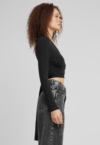 Melns garo piedurkņu crop top ar izsistām priekšējām daļām, apvienots ar augsto jostasvietu nedaudz novalkātiem melnas džinsa biksēm.