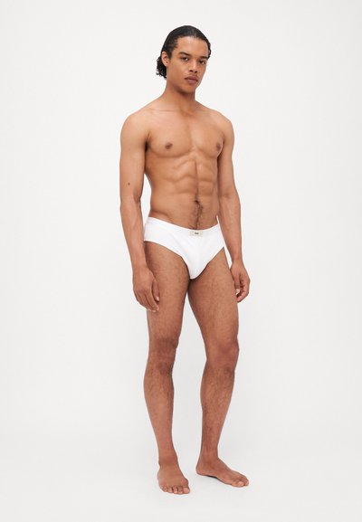 Caleçons blancs en coton avec une taille basse, affichant un design minimaliste et un petit logo gris sur la ceinture avant.