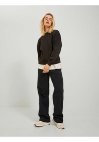 Black sweatshirt with a relaxed fit, ribbed cuffs, layered over a white top, paired with black wide-leg pants and beige sneakers.