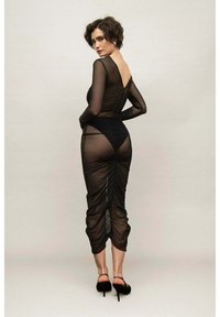 Czarna zwiewna sukienka z długimi rękawami, dopasowana sylwetka, marszczone detale z tyłu, długość do połowy łydki, w połączeniu z czarnymi szpilkami.