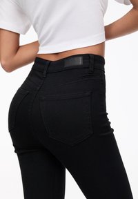 Jeans negros de cintura alta hechos de denim, con un corte ajustado, dos bolsillos traseros y una etiqueta de cuero negra en la cinturilla.