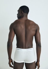 Weiße Boxershorts mit einem kontrastierenden grauen Calvin Klein-Logo am Bund, kombiniert mit glatter Haut, von hinten betrachtet.