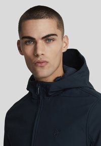 Giacca con cappuccio navy in tessuto morbido, dotata di chiusura con zip, logo ricamato sul petto e colletto alto per maggiore calore.