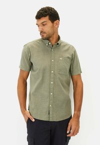 Kortærmet olivengrøn skjorte med knapper og lomme, struktureret stof og et subtilt mønster, båret sammen med sorte cargo shorts.