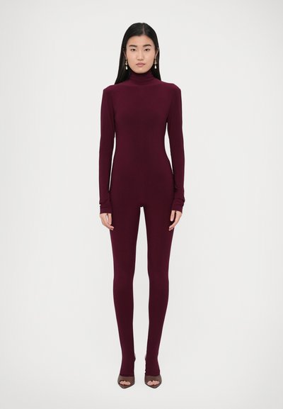 Weinroter Overall mit langen Ärmeln, hohem Kragen, figurbetontem Schnitt, elastischem Stoff und minimalen Details. Dazu braune offene Absätze getragen.