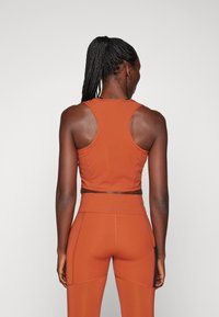 Sportski narančasti crop top s uskim trakama, uparen s odgovarajućim hlačama viskog struka koje ističu detalje šavova i elegantan dizajn.