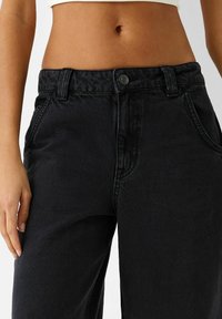 Musta farkkuhousut rentolla istuvuudella, joissa on nappisuljenta, etutaskut ja hieman haalistunut pinta.